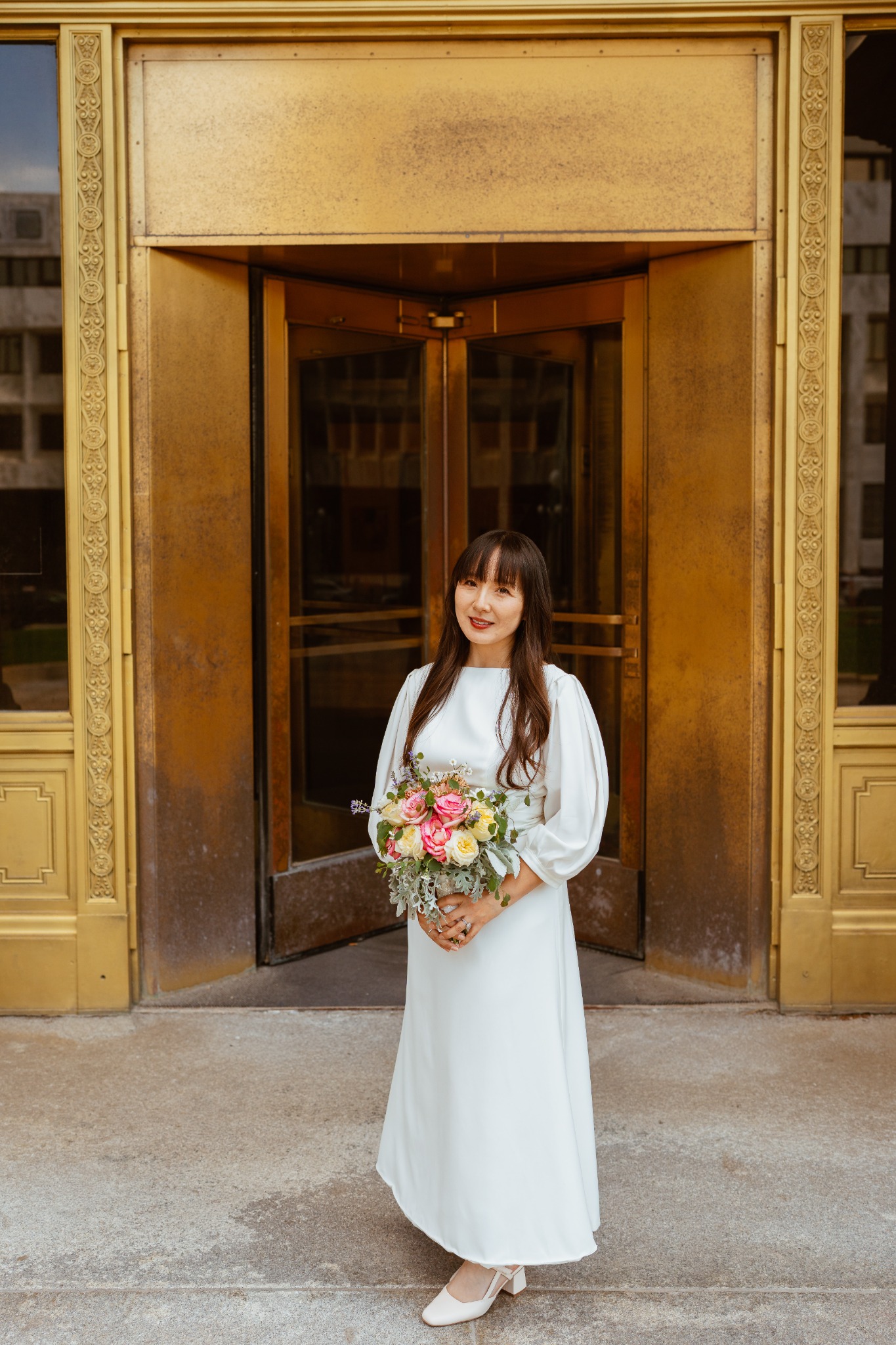 Bride standing with bouquet in front of a gold architectural doorway